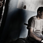 Mexikarra bere Martir Shreif gerla zaurituak zaintzen dituen zentroko gelako atean kanpora begira. Ahmed Hatari goes outside of his room in the War Victims (Andoni Lubaki / Ronak Press) CC-BY-ND-NC 2026