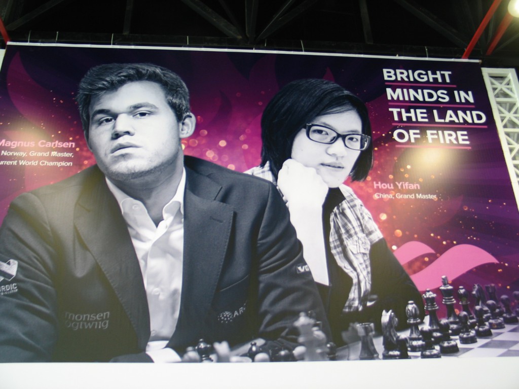 Cartel anunciador de la Olimpiada con los campeones del mundo, Magnus Carlsen y Yifán Hou, y el lema "mentes brillantes en la Tierra del Fuego L.G. 