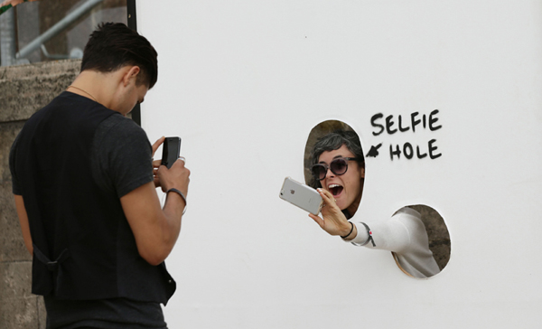 A visitor photographs herself through a 'selfie hole' at Banksy's biggest show to date, entitled 'Dismaland', during a press viewing in Western-super-Mare, Somerset, England, Thursday, Aug. 20, 2015. (Yui Mok/PA Wire via AP) UNITED KINGDOM OUT, NO SALES, NO ARCHIVE